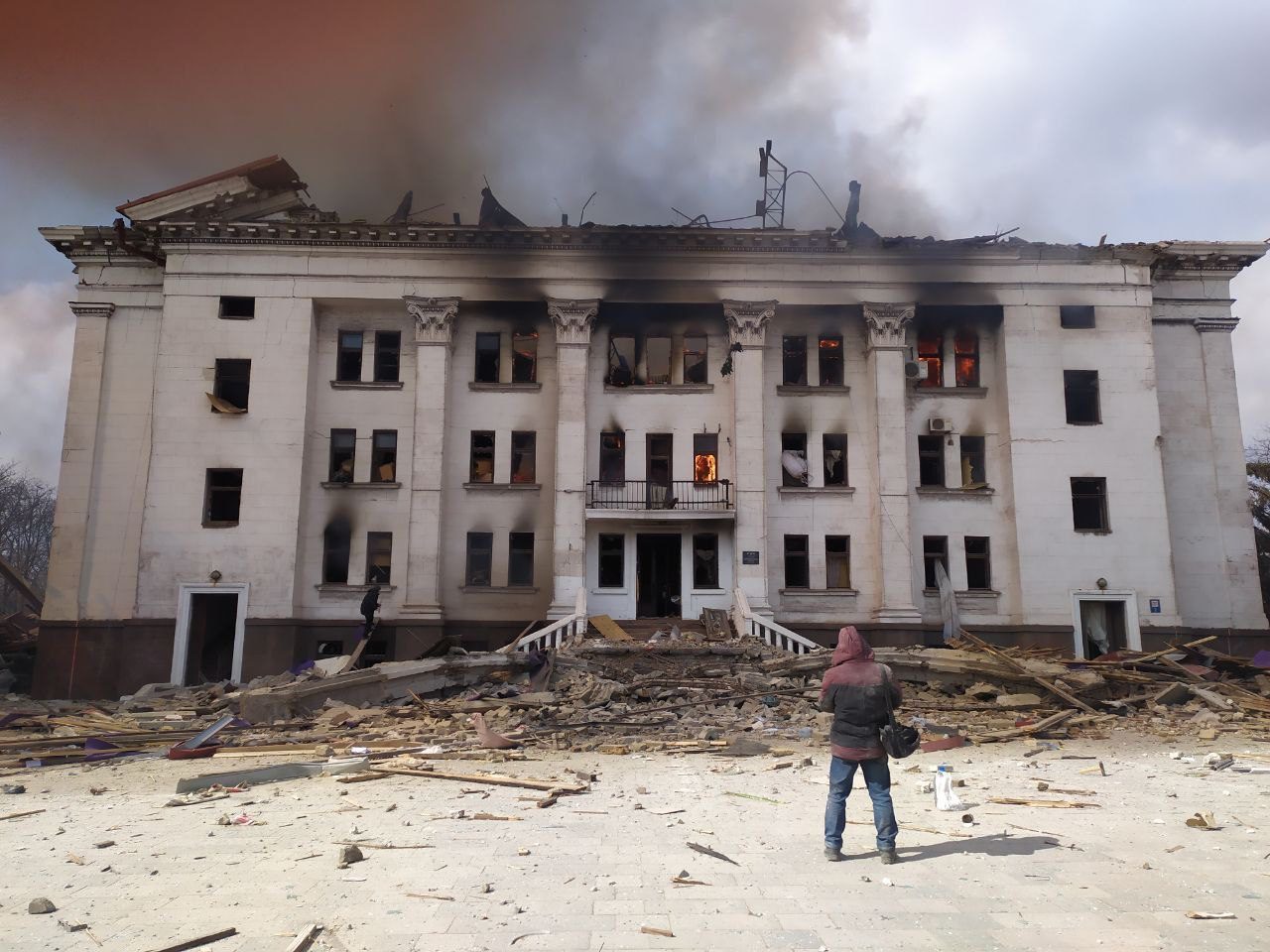 Zdjęcie frontu palącego się budynku Teatru Dramatycznego w Mariupolu. Pzed budynkim na placu stoi Serhij Zabohonskij. Mariupol, 16 marca 2022