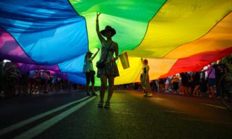 Members of Polish LGBTQ community are seen walking under a giant rainbow flag during the march.