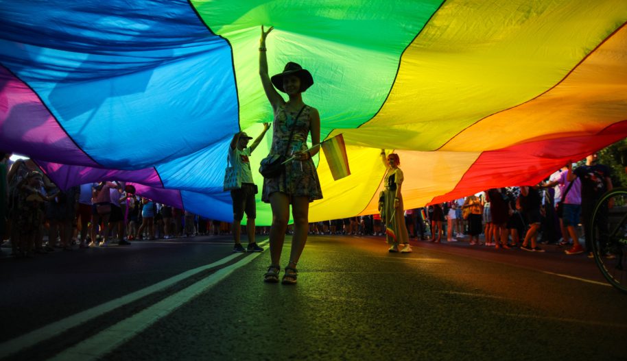 Members of Polish LGBTQ community are seen walking under a giant rainbow flag during the march.