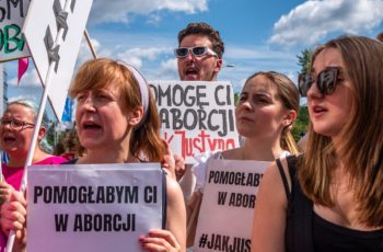 Protest solidarnościowy z Justyną Wydrzyńską pod sądem Warszawa-Praga, 14 lipca 2022. Osoby protestujące trzymają banery z hasłami: "Pomogę Ci w aborcji, jak Justyna"; "Pomogłabym Ci w aborcji".