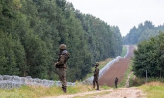 Żołnierze stojący naprzeciw drutów kolczastych na granicy.