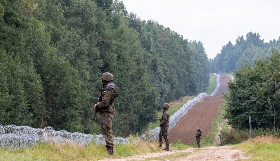Żołnierze stojący naprzeciw drutów kolczastych na granicy.