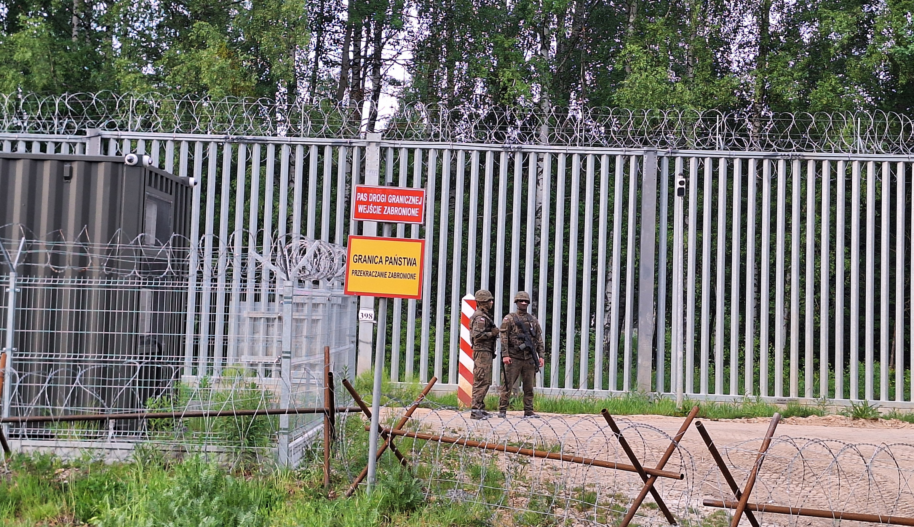 Dwóch żołnierzy stoi przy ogrodzeniu na polskiej granicy.